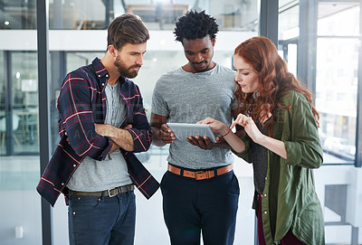 Buy stock photo Cropped shot of three young creatives working together on a digital tablet in a modern office