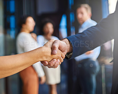 Buy stock photo Cropped shot of two unidentifiable businesspeople shaking hands with their coworkers in the background