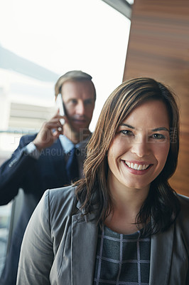Buy stock photo Portrait of a happy young businesswoman standing in her office with her coworker in the background