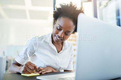 Buy stock photo Cropped shot of a young businesswoman writing notes while working on a laptop in a modern office