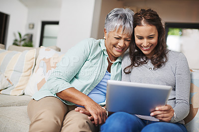 Buy stock photo Shot of a young woman showing something to her mother on her tablet while they sit on a sofa together