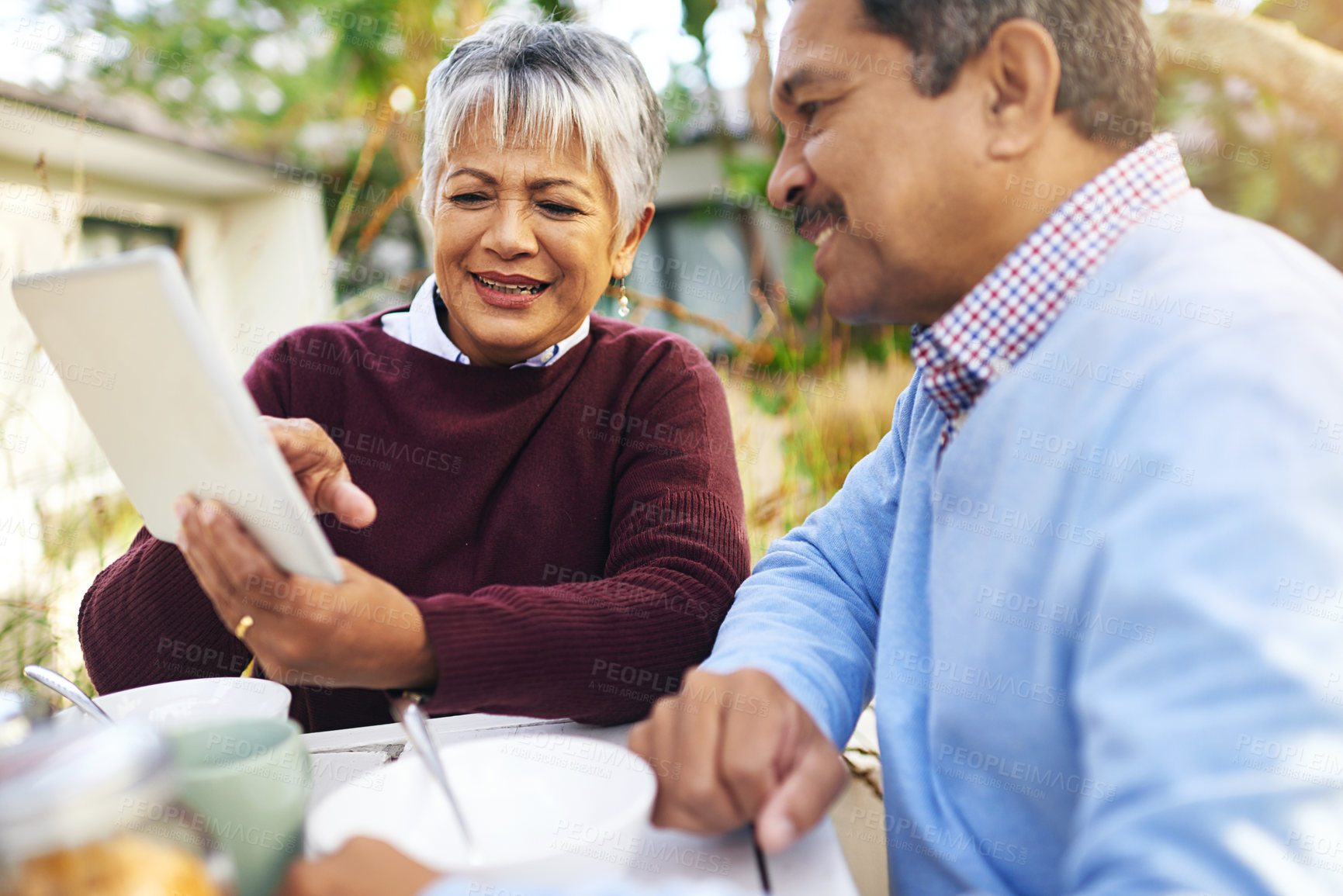 Buy stock photo Shot of an older couple using a digital tablet during a leisurely breakfast outdoors