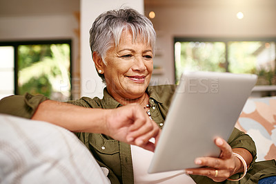 Buy stock photo Shot of a happy older woman relaxing on the sofa with her digital tablet at home