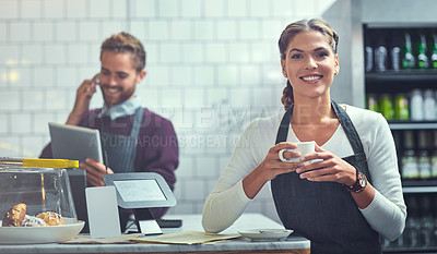 Buy stock photo Portrait of a young woman having coffee in her store while her coworker uses a digital tablet in the background