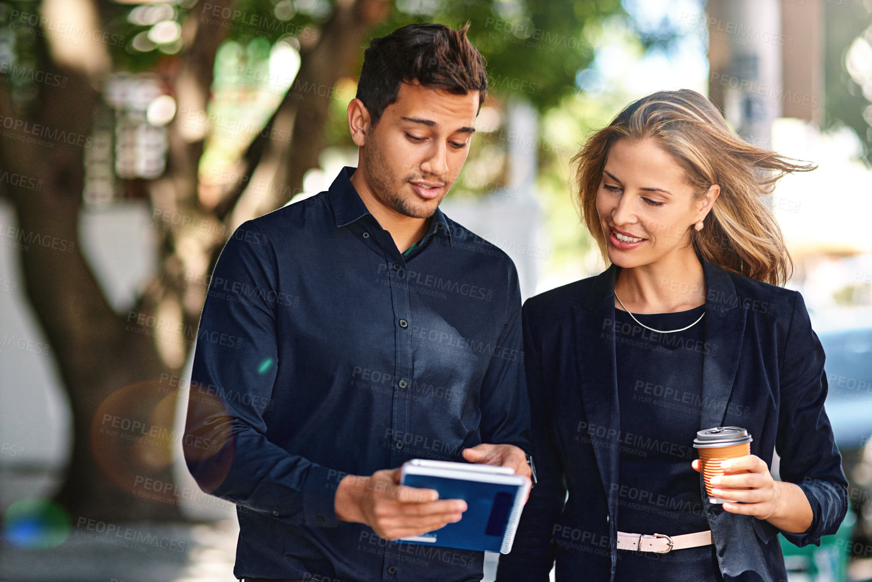 Buy stock photo Shot of two professional coworkers using a digital tablet together while walking outside
