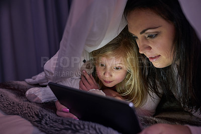 Buy stock photo Shot of a mother and daughter lying under a sheet reading a bedtime story on a digital tablet