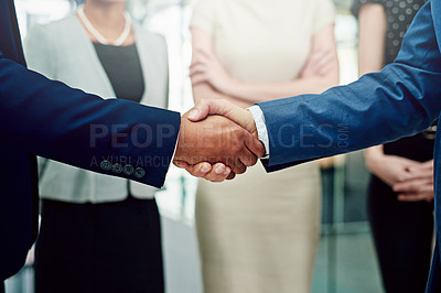 Buy stock photo Cropped shot of two unidentifiable businessmen shaking hands with their female coworkers in the background