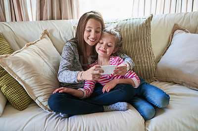 Buy stock photo Shot of two little girls playing with a smartphone while sitting on a sofa at home