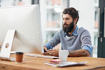 Buy stock photo Cropped shot of a young creative texting on a cellphone while sitting at a computer in an office