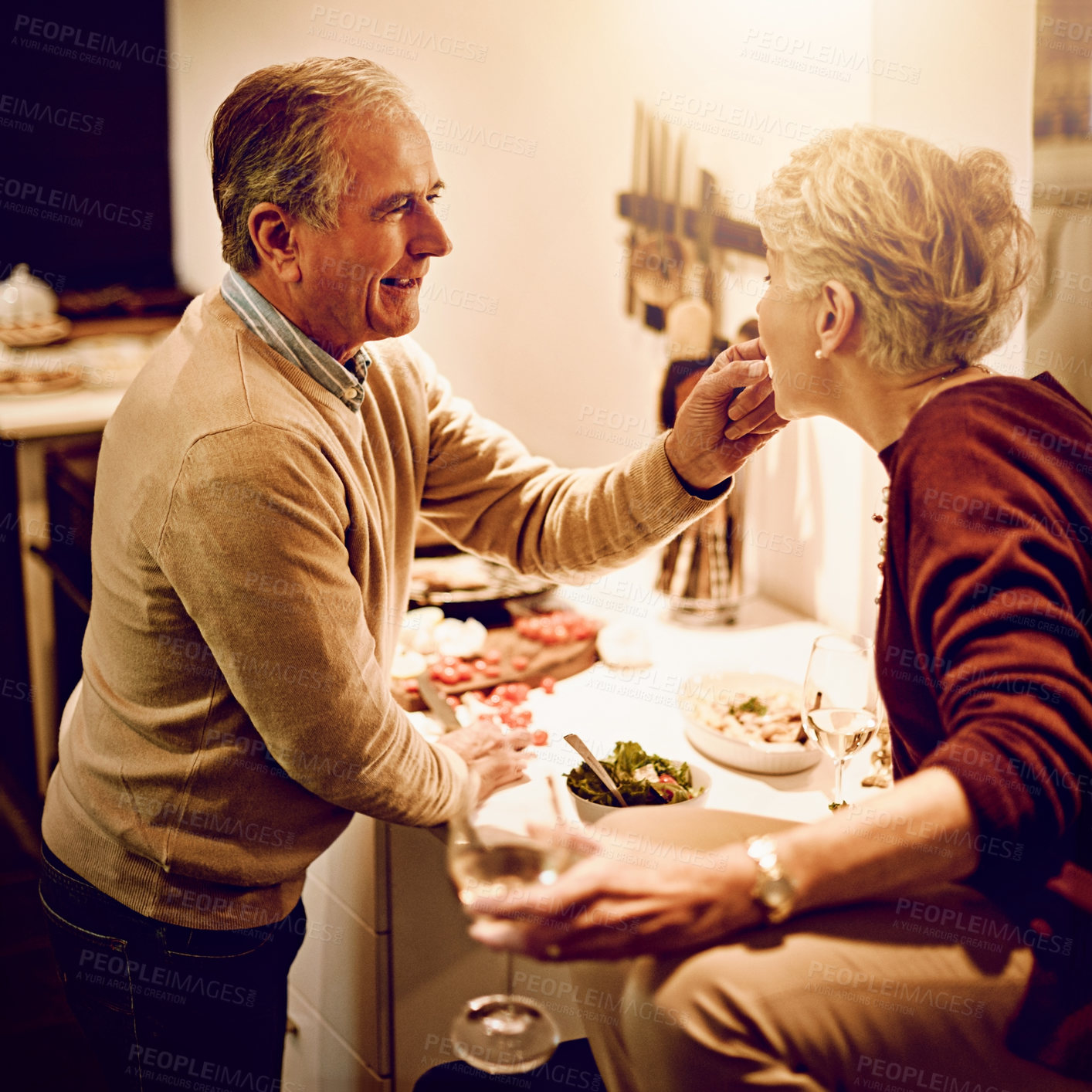 Buy stock photo Shot of an elderly man giving his wife something to taste while he cooks in the kitchen