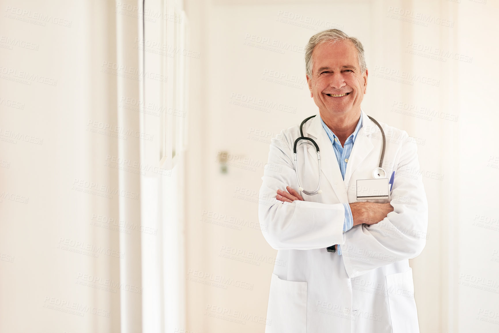 Buy stock photo Portrait of a mature doctor standing with his arms folded and smiling