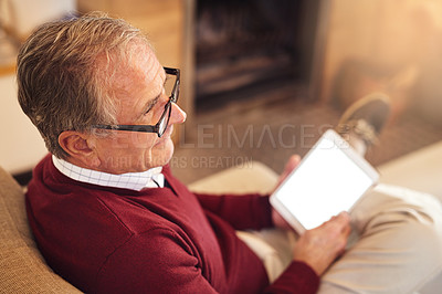 Buy stock photo Shot of a senior man using his digital tablet while sitting on a sofa