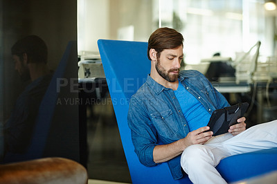 Buy stock photo Shot of a young businessman using a digital tablet while sitting in an office