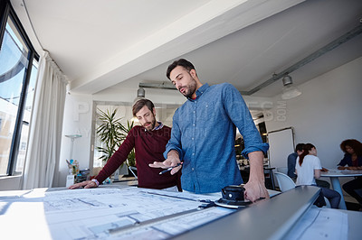 Buy stock photo Shot of two architects looking at blueprints together in their office