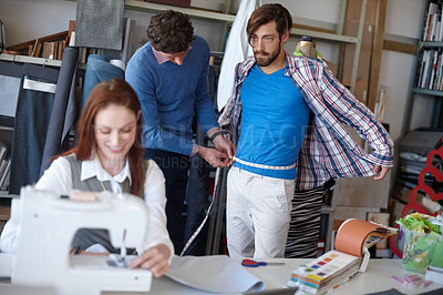 Buy stock photo Shot of a young fashion designer sewing while a colleague works with a client in the background
