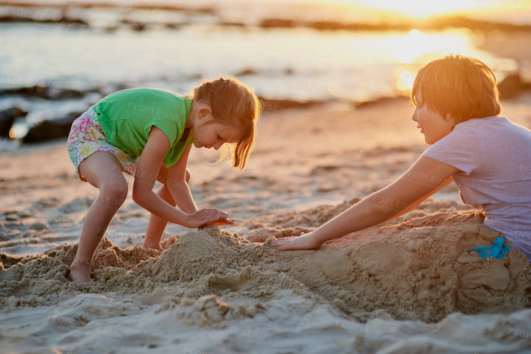 Buy stock photo Kids, creative in ocean and happy for building with sand, outdoor and vacation in sunset. Children, construction game and development in seashore, playful friends and together at beach for bonding