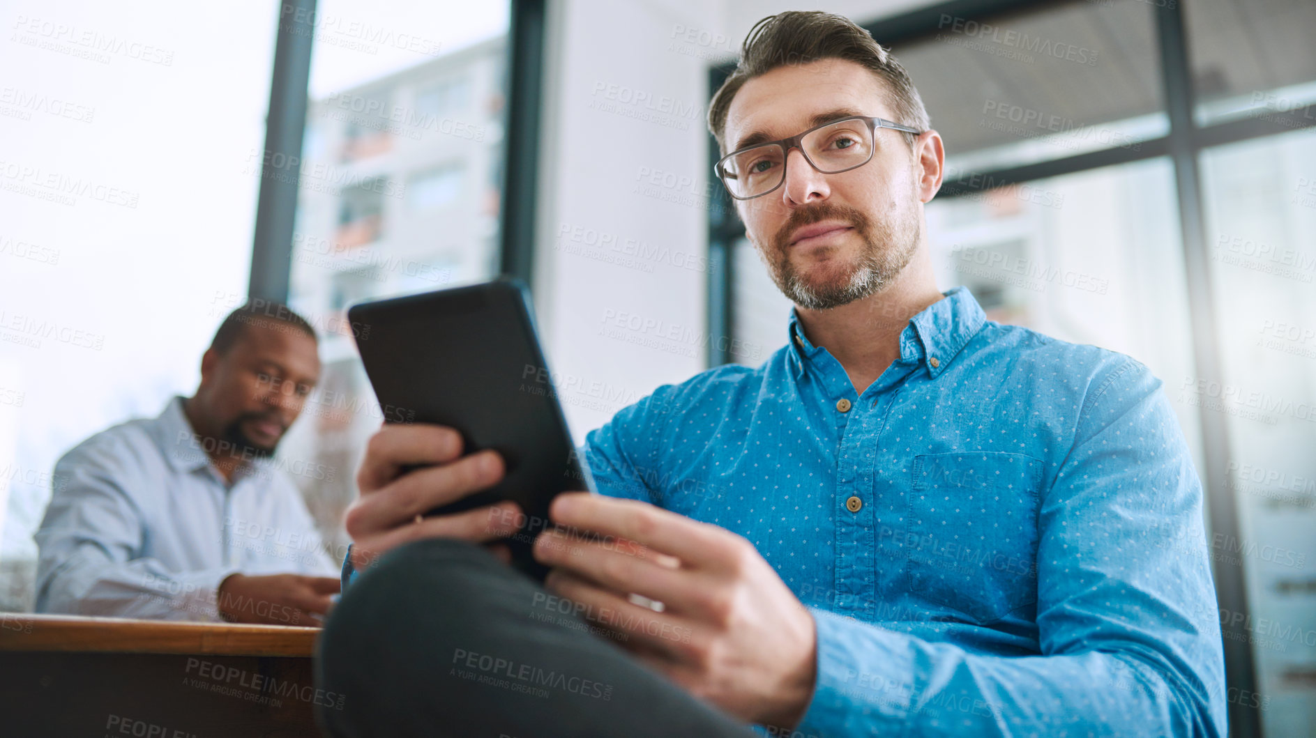 Buy stock photo Portrait of a businessman using his tablet with a colleague in the background