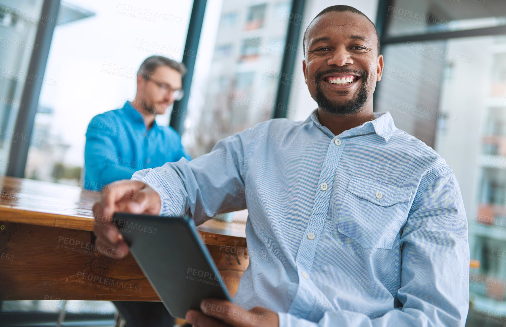 Buy stock photo Portrait of a businessman using his tablet with a colleague in the background