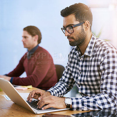 Buy stock photo Shot of a businessman working on his laptop with his colleagues blurred in the background