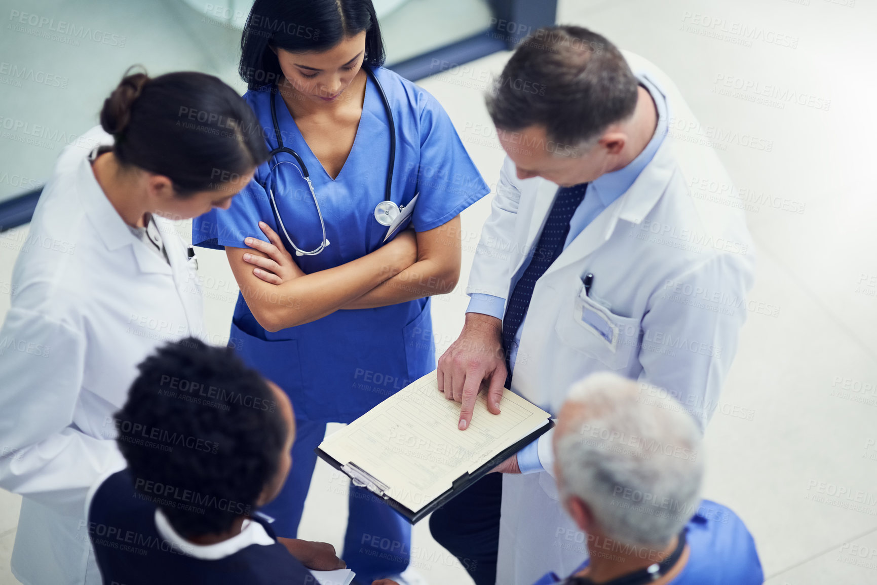 Buy stock photo Shot of a group of doctors talking together over a medical chart while standing in a hospital