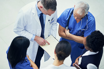 Buy stock photo Shot of a group of doctors talking together over a medical chart while standing in a hospital