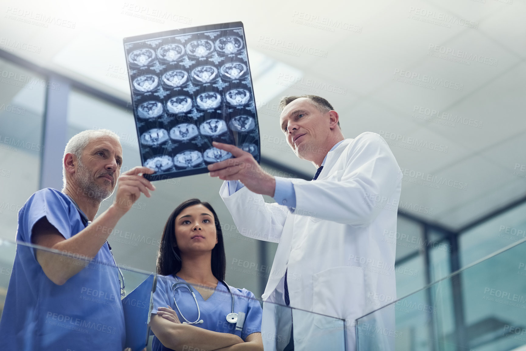 Buy stock photo Shot of a group of doctors looking at a medical scan while standing in a hospital
