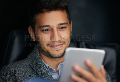 Buy stock photo Shot of a smiling young man using a digital tablet in the dark