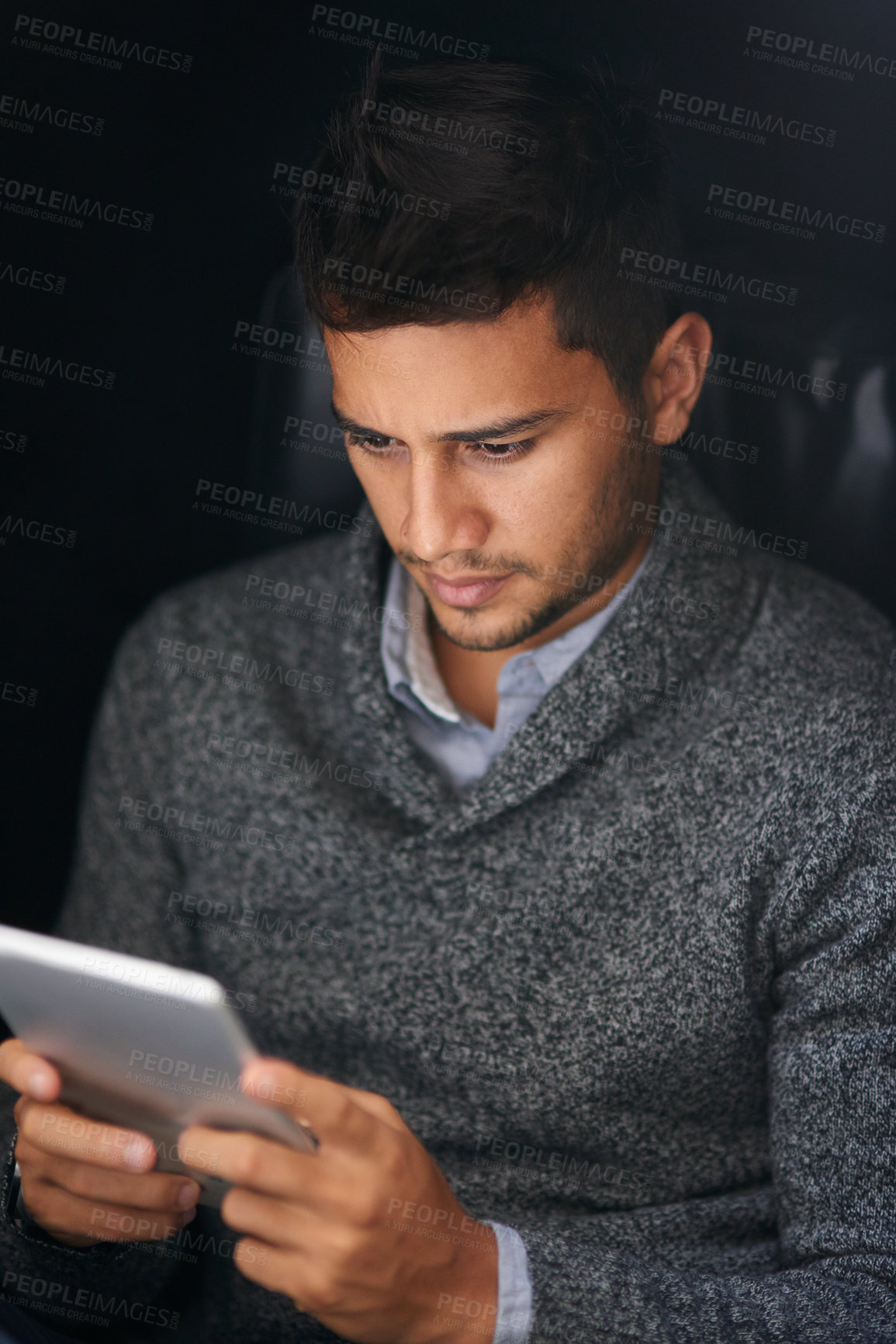 Buy stock photo Shot of a young man using a digital tablet in the dark