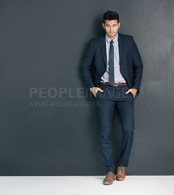 Buy stock photo Studio shot of a young businessman standing with his hands in his pockets against a gray background
