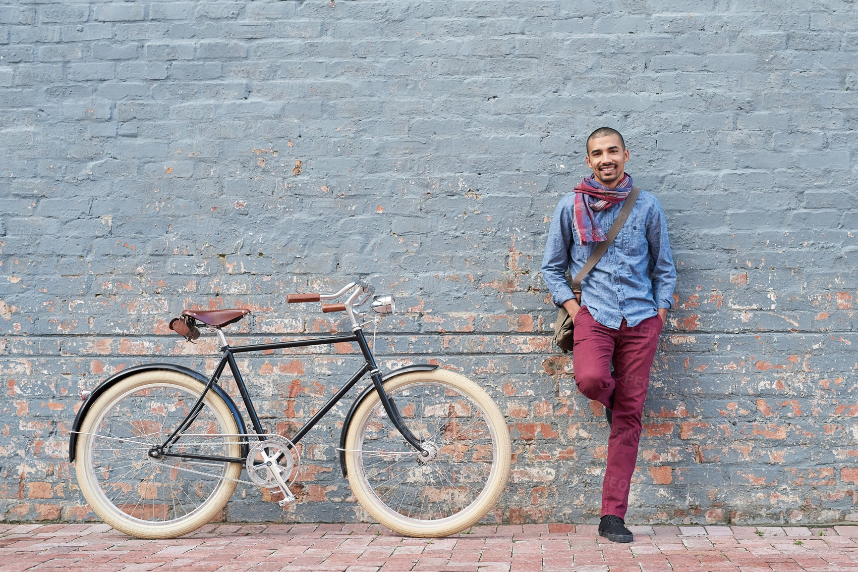 Buy stock photo Portrait of a young man posing with his bicycle against a grey wall in the city