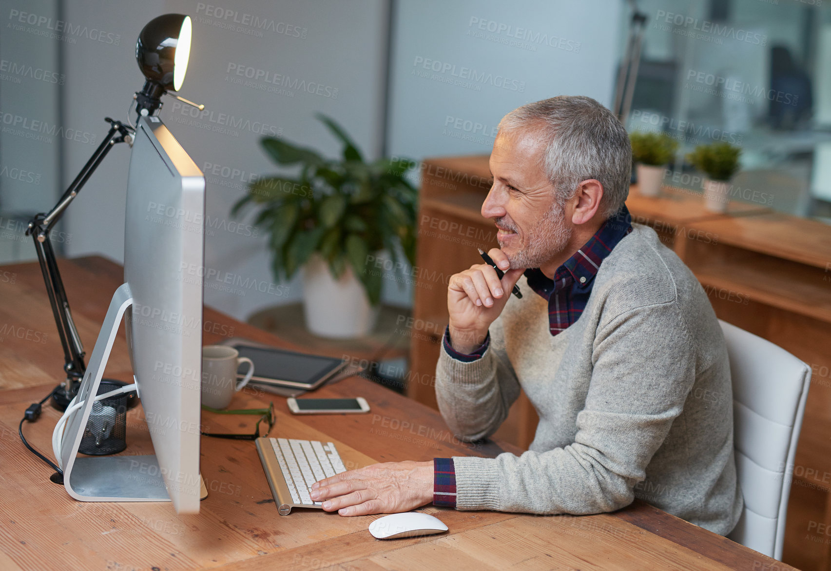 Buy stock photo Shot of a smiling mature businessman working on a computer in an office