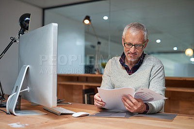 Buy stock photo Shot of a smiling mature businessman reading paperwork while sitting at his desk in an office