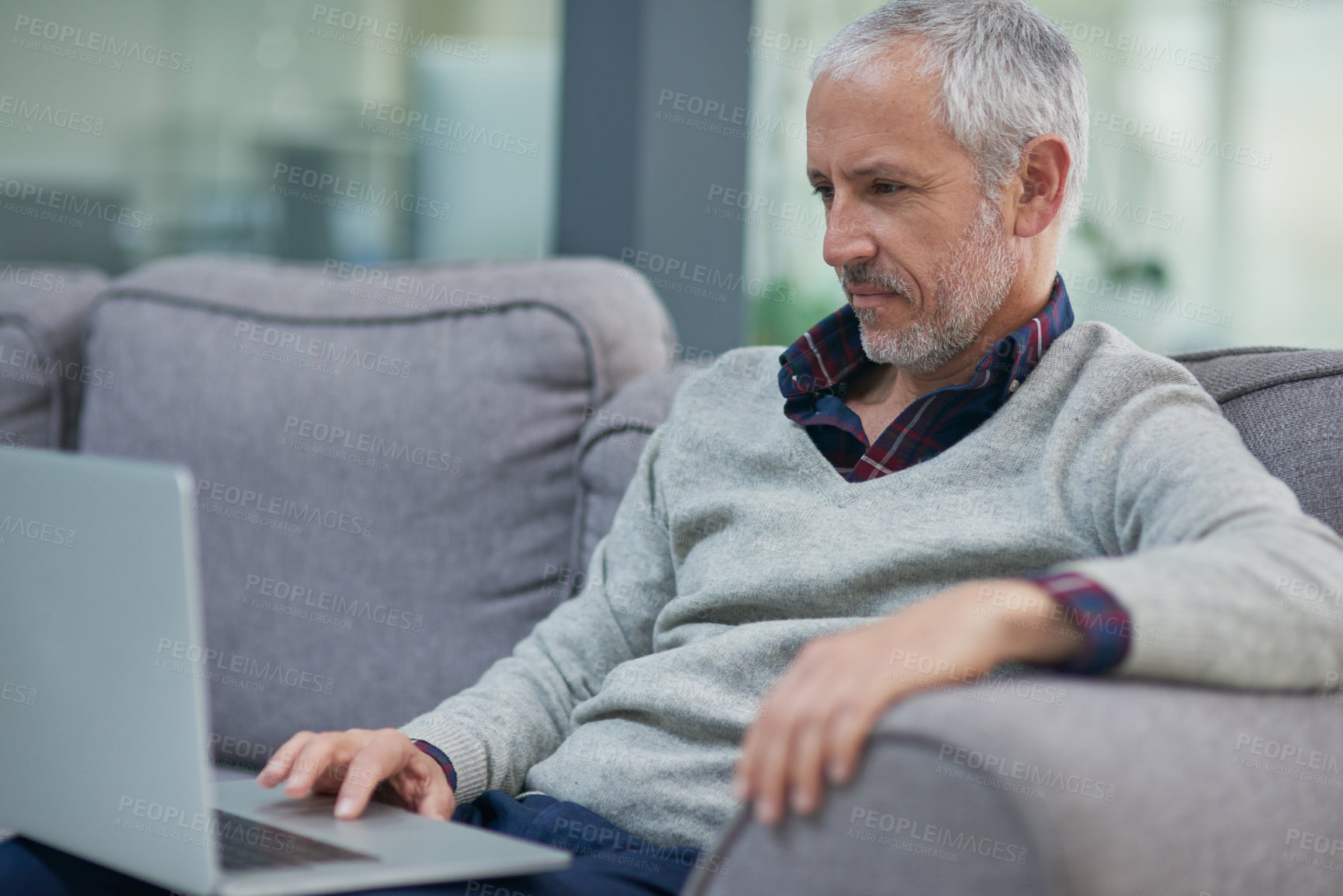 Buy stock photo Shot of a mature businessman using a laptop while sitting on a sofa in an office