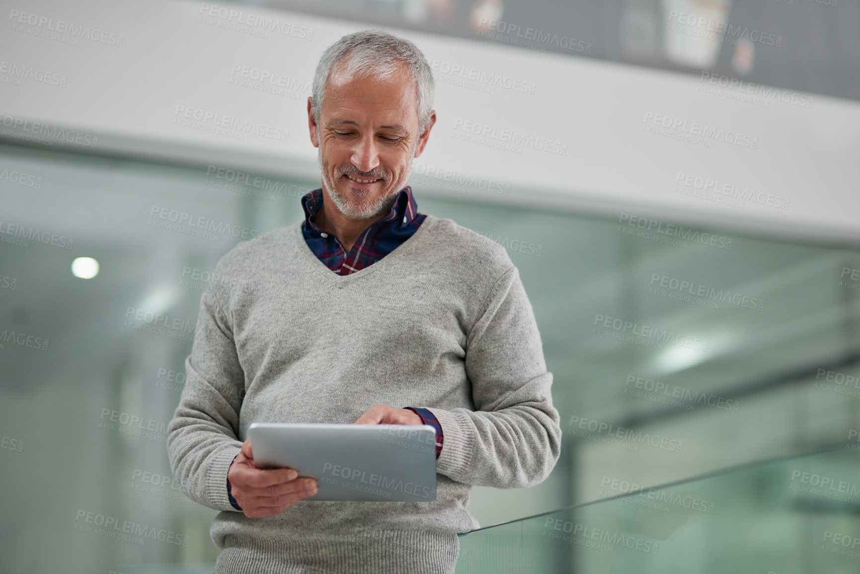 Buy stock photo Shot of a mature businessman using a digital tablet while standing in an office