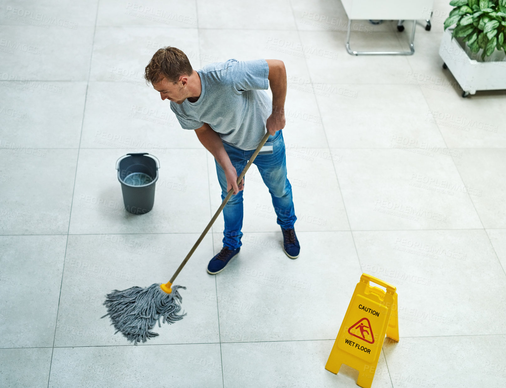 Buy stock photo High angle shot of a young man mopping the office floor
