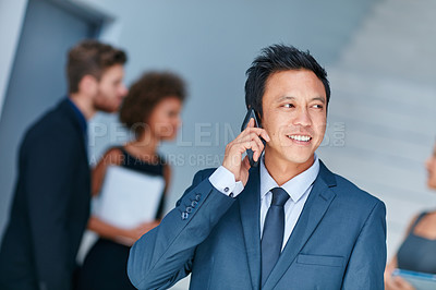 Buy stock photo Cropped shot of a young businessman talking on a cellphone with colleagues in the background