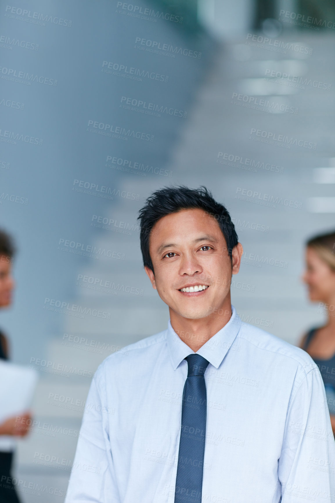 Buy stock photo Portrait of a young businessman standing in an office with colleagues in the background