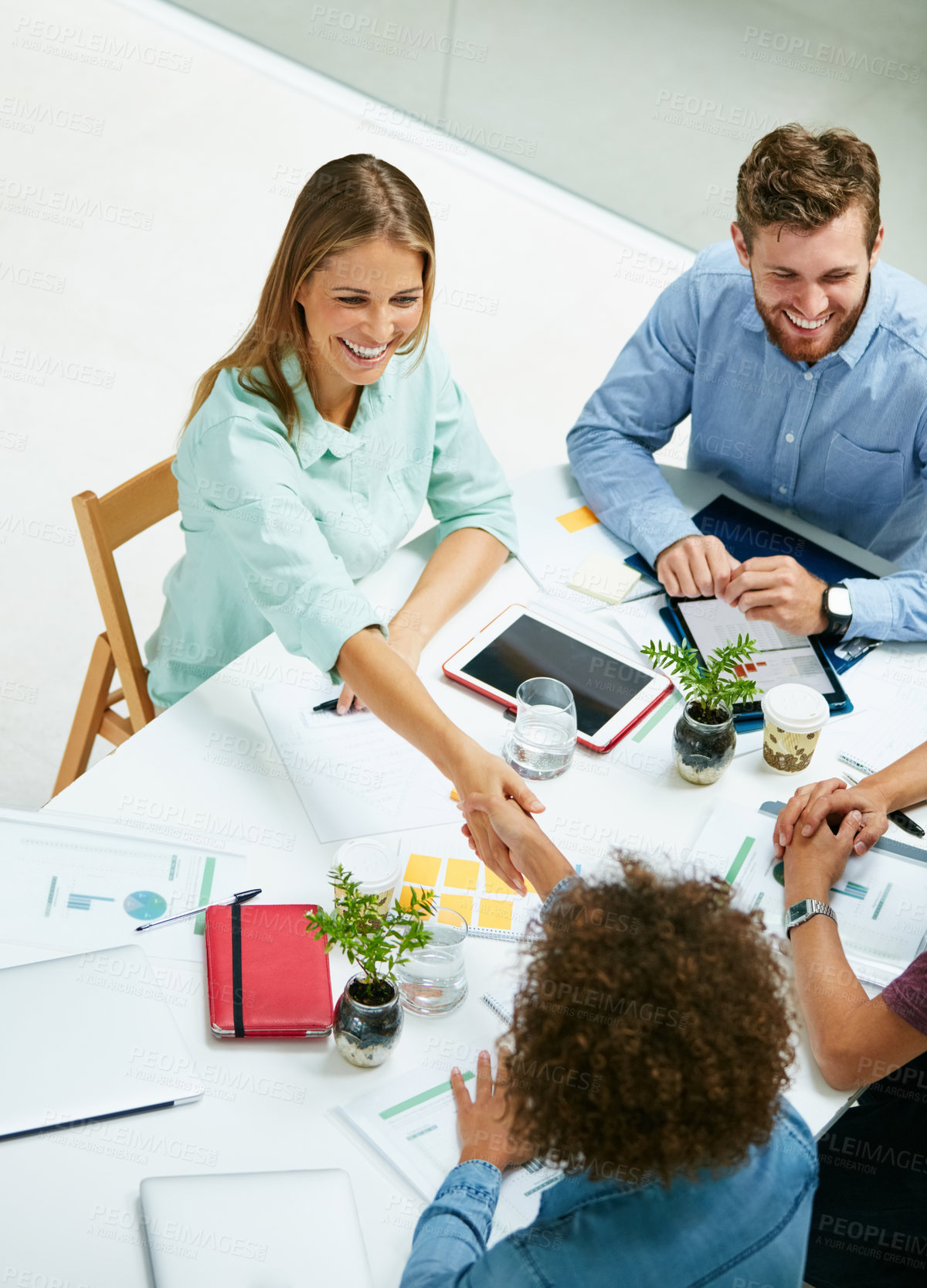 Buy stock photo High angle shot of two businesspeople shaking hands together at a table in an office while colleagues look on