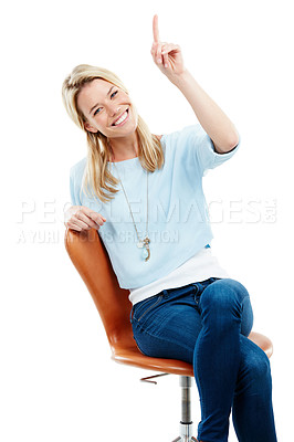 Buy stock photo Studio portrait of a happy young woman sitting on a chair pointing at copyspace against a white background