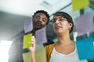 Buy stock photo Shot of two colleagues working with adhesive notes on a glass wall in the office