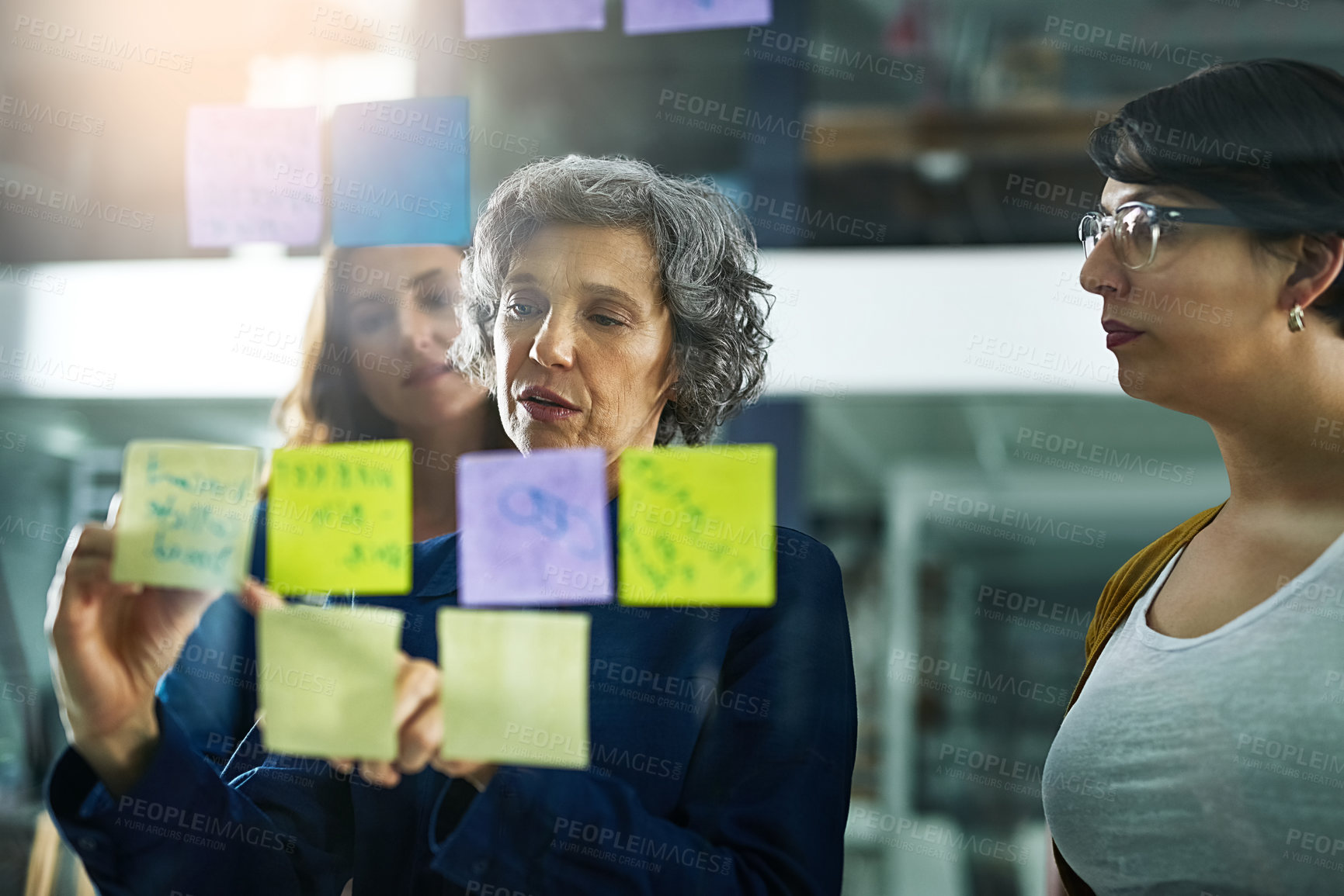 Buy stock photo Shot of a group of colleagues working with adhesive notes on a glass wall in the office