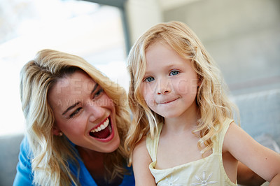 Buy stock photo Shot of a young mother and her daughter laughing while sitting on the sofa at home