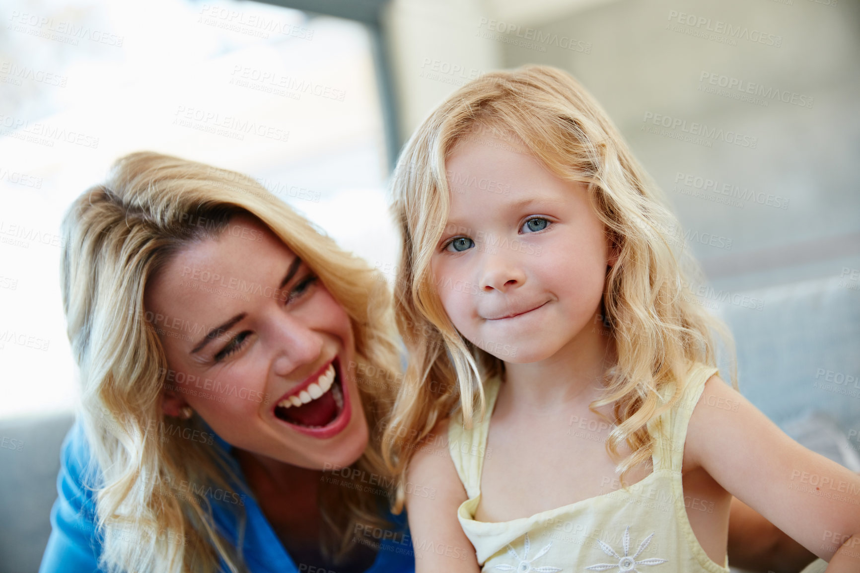 Buy stock photo Shot of a young mother and her daughter laughing while sitting on the sofa at home