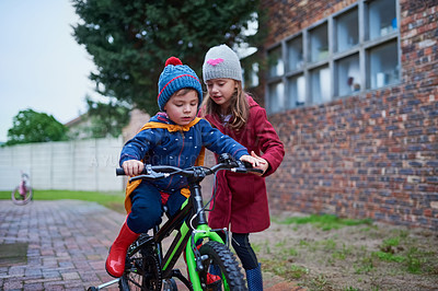 Buy stock photo Cropped shot of a little girl teaching her brother how to ride a bicycle outside