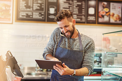 Buy stock photo Cropped shot of a business owner using a digital tablet while taking on a cellphone in his cafe