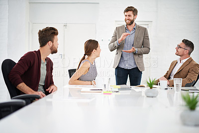 Buy stock photo Shot of a businessman giving a presentation to colleagues sitting at a table in a modern office