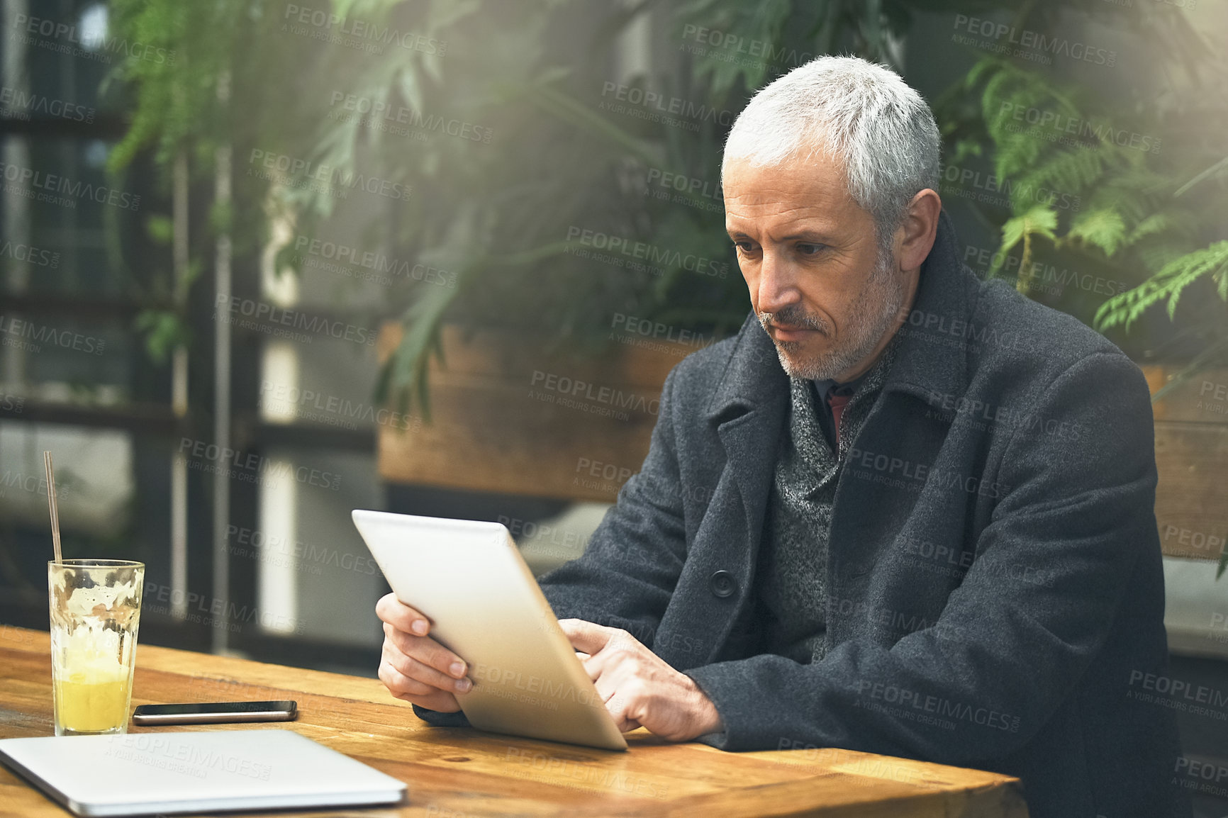 Buy stock photo Shot of a mature businessman using his tablet in a cafe