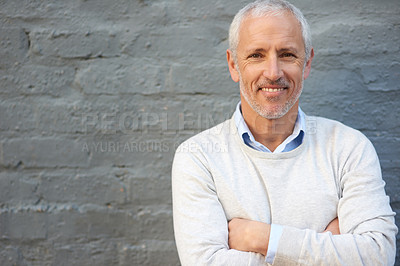 Buy stock photo Portrait of a mature businessman standing with his arms folded against a brick wall