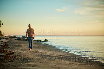Buy stock photo Shot of a man going for a walk along the water’s edge at the beach