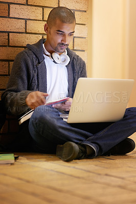 Buy stock photo Shot of a college student using his laptop while sitting in a hallway at campus